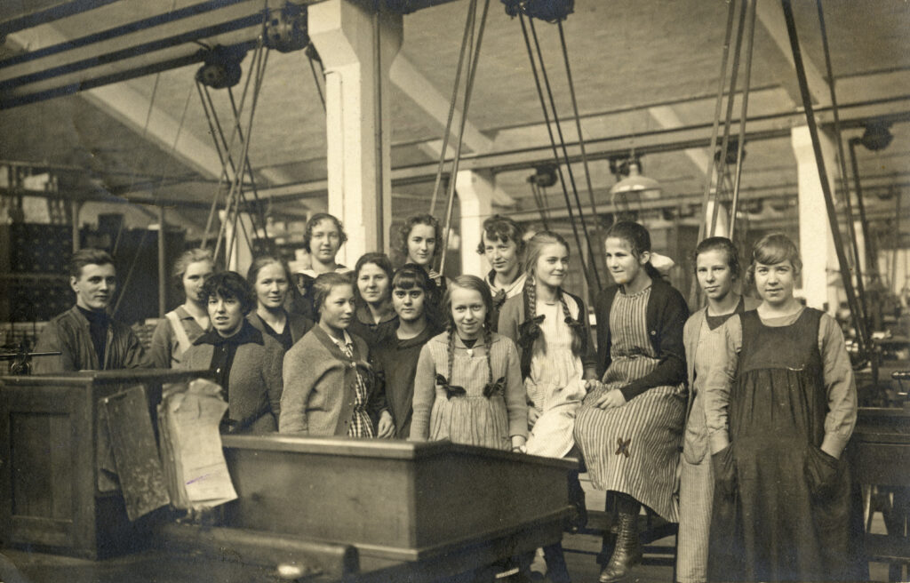 En grupp unga kvinnor och en förman står uppställda i en verkstad.