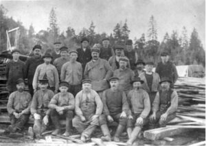 svartvitt foto av tjugotvå män uppställda framför brädhögar.