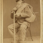 Ett porträttfotografi av man med långt skägg sitter på en stol.