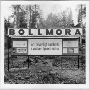 En skylt i en skogsbacke med namnet BOLLMORA i stora bokstäver. Under så står det "ett bilvänligt samhälle i vacker Tyresö-natur". Kartor och mer information i mindre bokstäver kan inte uskiljas i detalj på bilden.