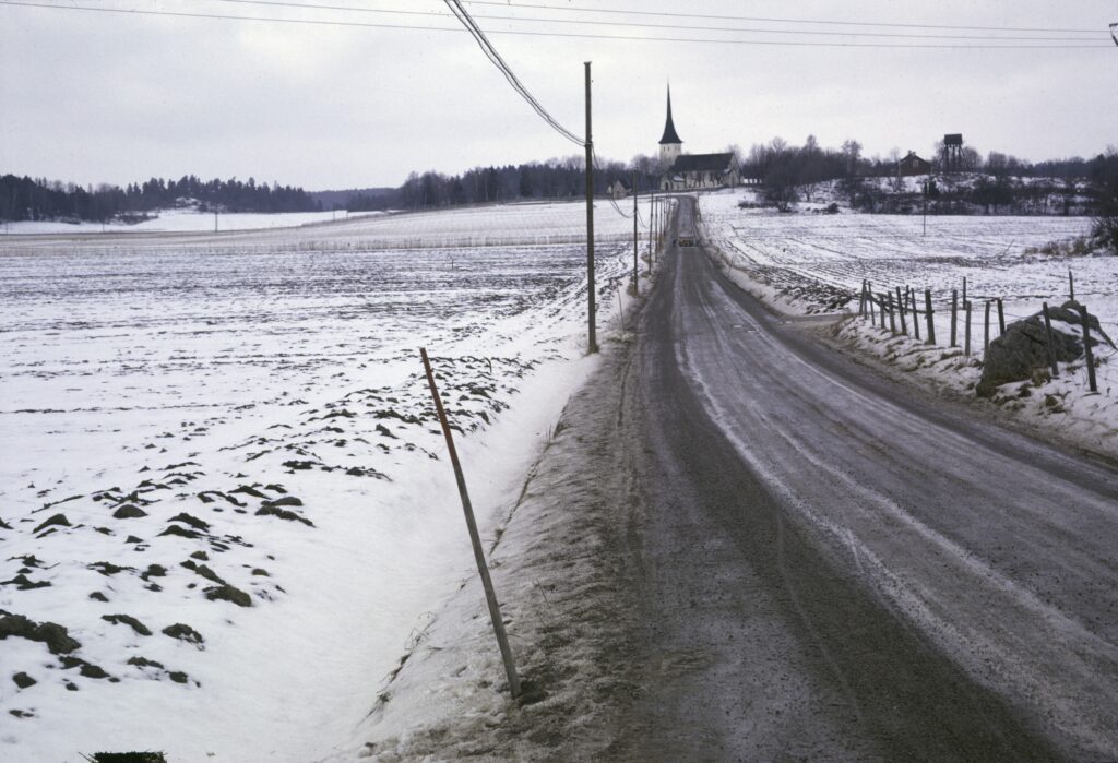 En blöt väg mellan snöpudrade åkrar leder fram mot Sånga kyrka.