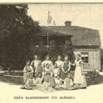 Tretton flickor står uppställda framför Glömsta gård tillsammans med sin föreståndarinna. Texten under bilden lyder: Från barnhemmet vid Glömsta.