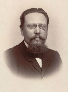 Ett ateljéfoto av en man med skägg och glasögon.