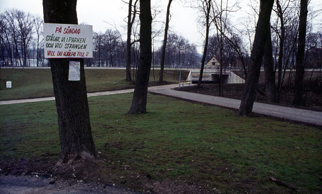 Ett plakat på ett träd i parken lyder: På söndag städar vi parken och vid stranden. Vill du hjälpa till?