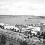 Ett svartvitt foto från hög höjd som visar tågspåren och några industribyggnader.