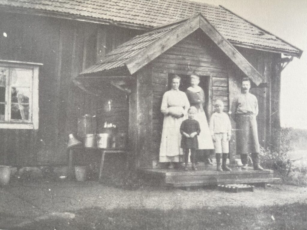 Två barn och tre vuxna på trappen till ett torp.