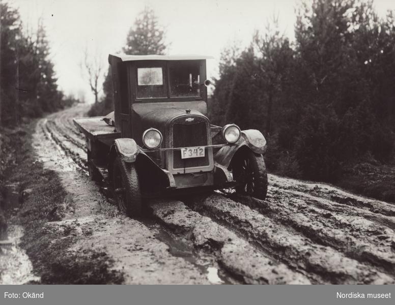 Ett svartvitt foto av en gammal bil som kör på en lerig väg.