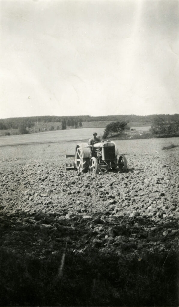 Ett svartvitt foto av en man på en traktor utan förarhytt på en åker.