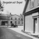 Ett svartvitt vykort av Sigtunas torg. En gammaldags öppen bil står i stolskenet mitt på torget.