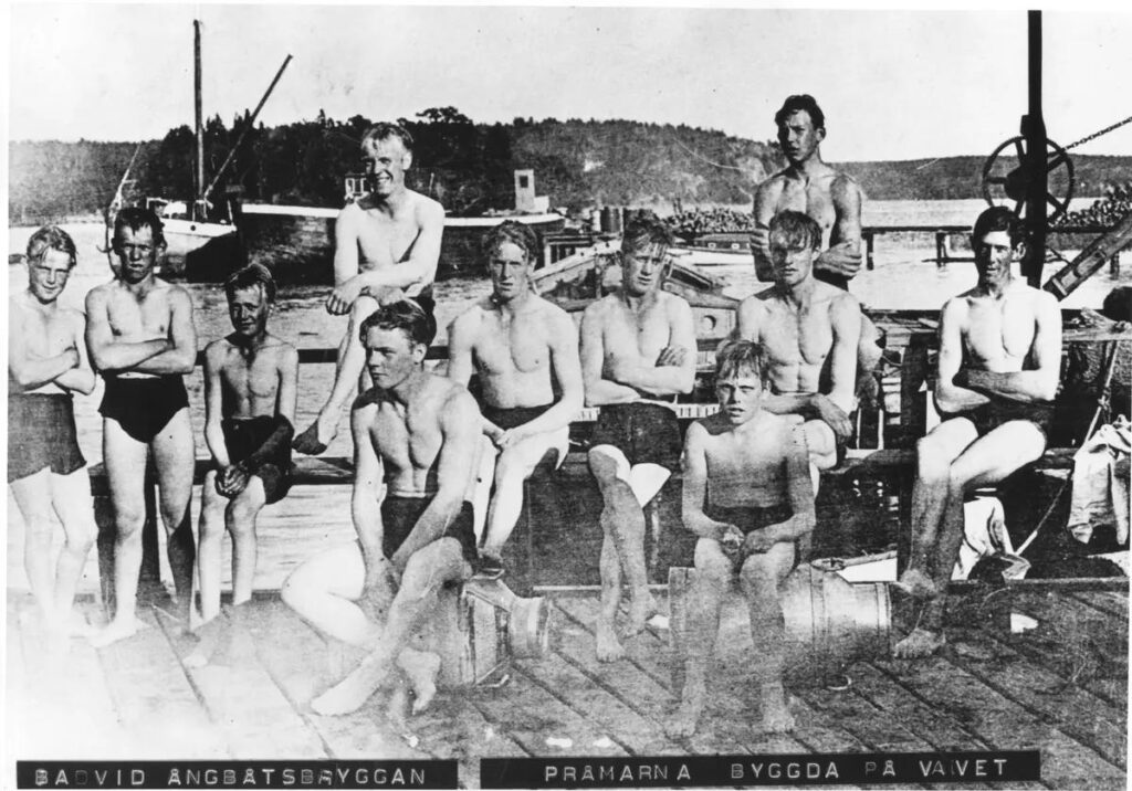 Ett svartvitt foto av elva pojkar i badbyxor på en pråm.