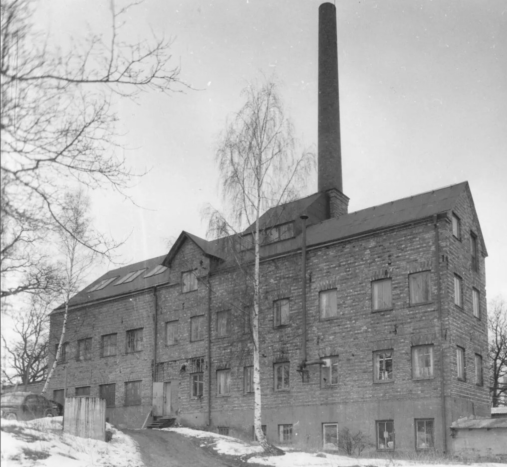 En svartvit bild av en tegelfabrik i tre våningar med hög skorsten.