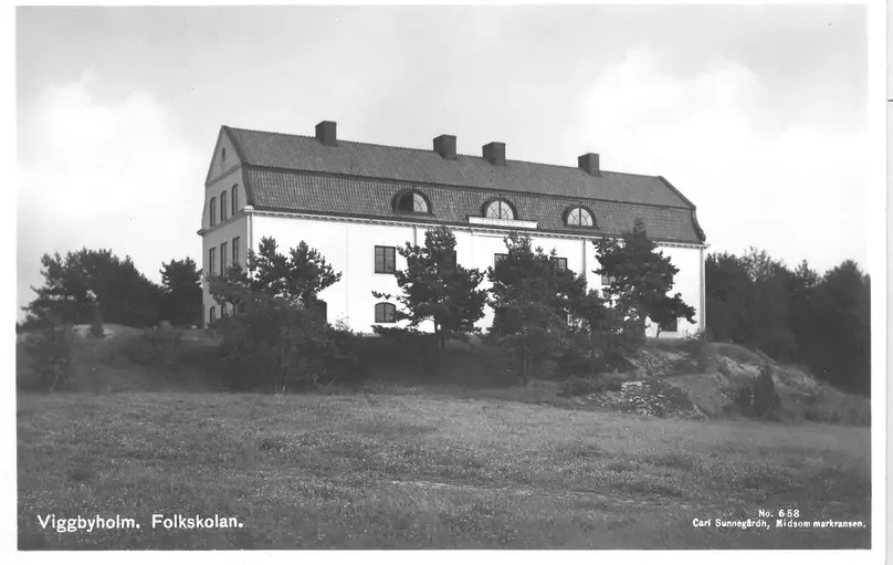 Ett svartvitt vykort med den ljusa skolbyggnaden i sten och två våningar på en höjd.